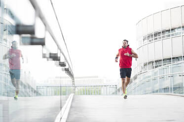 Junger Mann joggt auf einer Fußgängerbrücke in der Stadt - DIGF11799