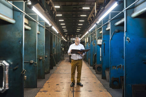 Älterer Geschäftsmann mit Ordner in einer Fabrikhalle, lizenzfreies Stockfoto