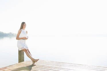 Young woman relaxing with cup of coffee on jetty - DIGF11919