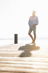 Young man standing on a jetty at backlight - DIGF11929