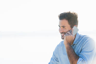 Portrait of smiling young man on the phone at backlight - DIGF11931