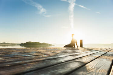 Junger Mann sitzt auf der Promenade am See und genießt den Sonnenaufgang - DIGF11951