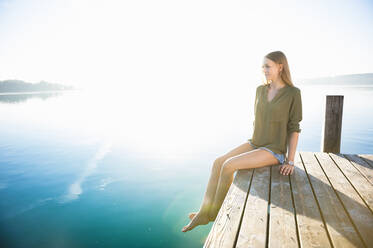 Junge Frau sitzt auf einem Steg am See bei Sonnenaufgang - DIGF11956
