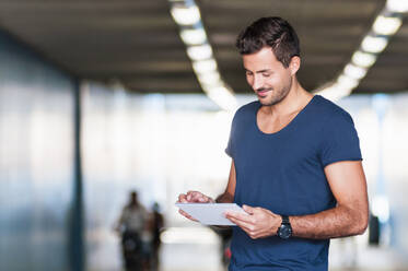 Smiling young man standing in an underpass using digital tablet - DIGF11978