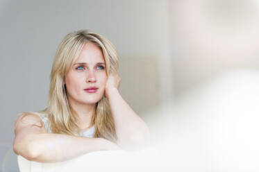 Porträt einer nachdenklichen blonden Frau mit blauen Augen, die sich an eine Rückenlehne lehnt - DIGF12008