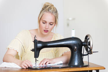 Porträt einer blonden jungen Frau an einer alten Nähmaschine - DIGF12017