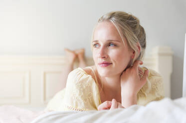 Porträt einer lächelnden blonden Frau mit blauen Augen auf dem Bett liegend - DIGF12024