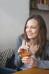Porträt einer lächelnden Frau, die in einem Café einen Smoothie trinkt und in die Ferne schaut - DIGF12026