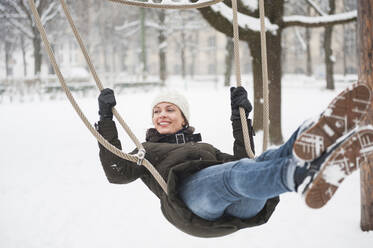 Porträt einer glücklichen Frau auf einer Schaukel im Winter - DIGF12032