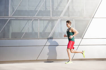 Mid adult man running on sidewalk by modern building in city - DIGF12039