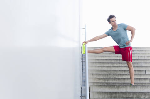 Handsome mid adult man stretching leg on wall while standing over steps stock photo