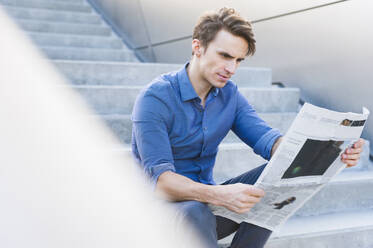 Selbstbewusster gut aussehender Geschäftsmann, der auf einer Treppe sitzend Zeitung liest - DIGF12051