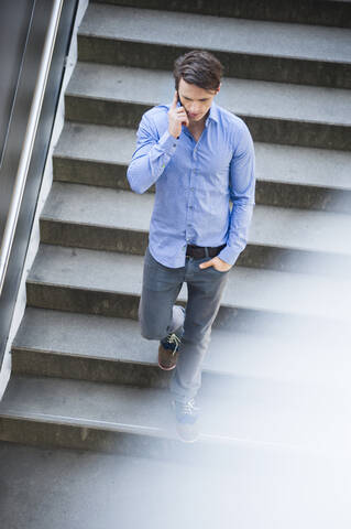 Businessman talking over smart phone while moving down on steps stock photo
