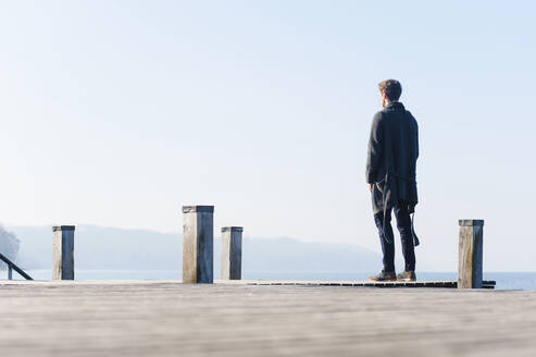 Mann schaut auf den See gegen den klaren Himmel, während er an einem sonnigen Tag auf dem Pier steht - DIGF12056