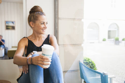 Porträt einer lachenden Frau mit Brötchen, die in einem Café sitzt und aus dem Fenster schaut - DIGF12057
