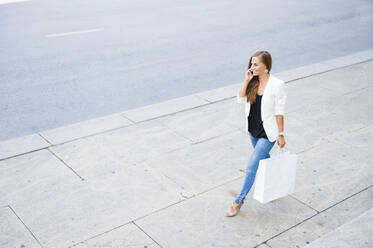 Smiling woman on the phone walking on pavement with shopping bag - DIGF12067