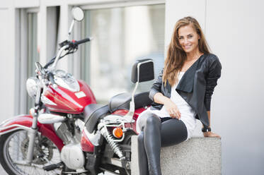 Portrait of smiling woman sitting in front of motorbike in the city - DIGF12074
