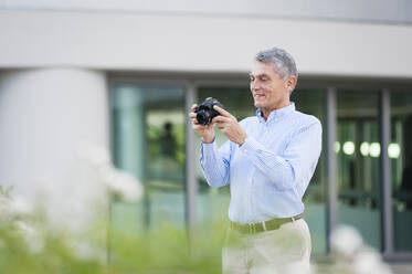 Portrait of smiling senior businessman with digital camera outdoors - DIGF12076