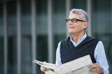 Portrait of smiling senior businessman with newspaper outdoors - DIGF12078