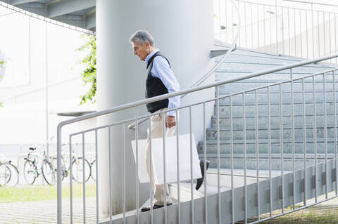 Senior man with shopping bags walking downstairs stock photo