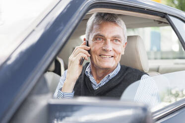 Porträt eines lächelnden älteren Geschäftsmannes beim Telefonieren im Auto - DIGF12083