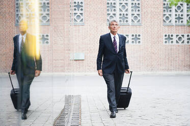 Portrait of senior businessman pulling trolley bag on a square - DIGF12090