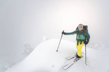 Young woman smiling backcountry skiing on snowy summit in Squamish - CAVF82166