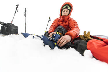 Niedriger Winkel eines Mannes, der mitten im Schnee seine Skischuhe anzieht - CAVF82168