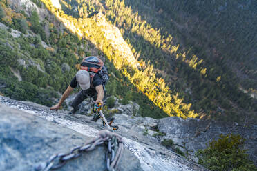 Mann mit Hut, der nach unten schaut, jongliert Seil mit Rucksack am El Capitan hoch - CAVF82244