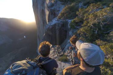Three hikers looking at The Nose El Capitan from the top at sunset - CAVF82248