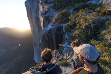 Three hikers looking at The Nose El Capitan from the top at sunset - CAVF82249