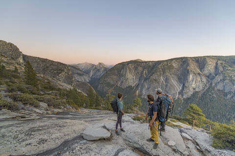 Three hikers looking at Half Dome from El Capitan sunset Yosemite stock photo