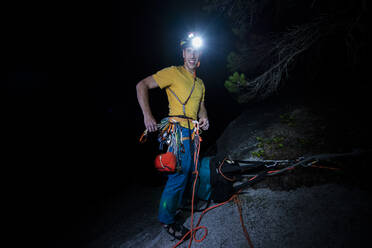 Mann beim nächtlichen Klettern mit Stirnlampe auf dem Gipfel des Berges - CAVF82267