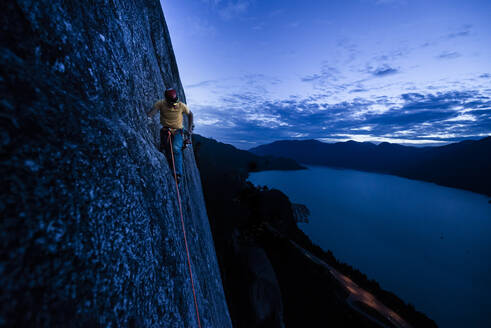 Side view man rock climbing at night above the sea and highway - CAVF82273