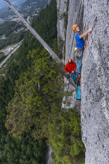 Zwei Männer beim Klettern und Sichern an einem hängenden Baum in einer ausgesetzten Wand - CAVF82303