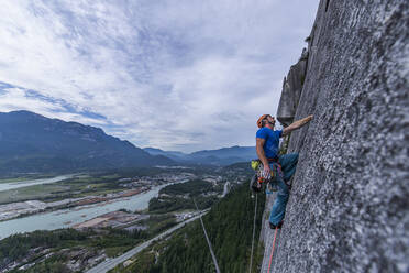 Man looking up while rock climbing Squamish Chief on granite with view - CAVF82305