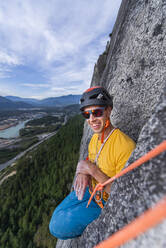 Mann sitzend in lustiger Position beim Klettern mit Helm und Sonnenbrille - CAVF82311