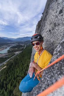 Mann sitzend in lustiger Position beim Klettern mit Helm und Sonnenbrille - CAVF82311