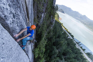 Mann klettert im Vorstieg auf Granit in Squamish mit Blick auf den Ozean im Hintergrund - CAVF82330