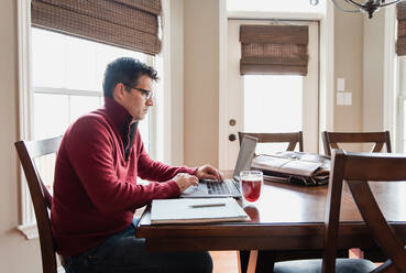 Man in glasses working from home using a computer at a dining table. - CAVF82344