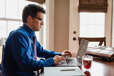 Man in shirt and tie working from home using computer at dining table. - CAVF82346