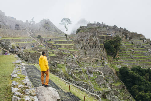 Ein Mann in einer gelben Jacke steht in der Nähe der Ruinen von Machu Picchu, Peru - CAVF82412