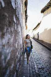A young woman is standing near an old wall in Cusco, Peru - CAVF82425