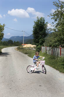 Ein kleiner Junge fährt mit dem Fahrrad auf einer leeren Straße in den Mounains - CAVF82442