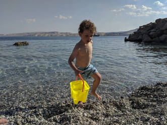 Kleiner Junge trägt eine hellgelbe Wasserbleiche am Meer - CAVF82445