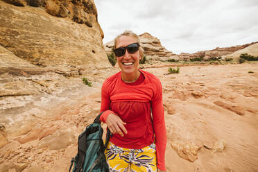 Desert hiker with slanted sunglasses and messup up shirt laughing - CAVF82450