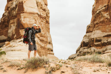 Hiker with big backpack pauses under red rock structures in Utah - CAVF82452