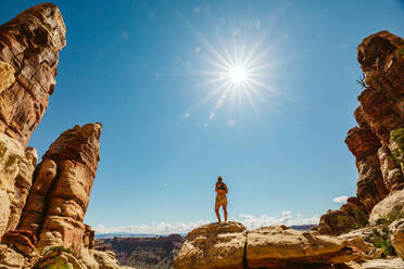 Woman in sports bra and shorts stands on rocks in desert under sun - CAVF82486