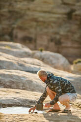 Blonder Mann schöpft Wasser aus einer flachen Pfütze in der Wüste - CAVF82504