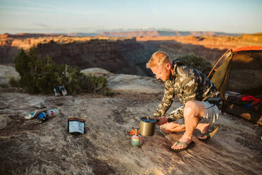 Male camper boils water with a whisper light at camp in desert - CAVF82508